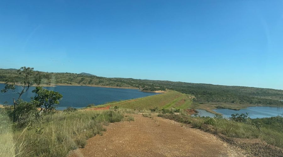 Represa da fazenda vista do alto do barramento, com a crista de terra atravessando o quadro, água nos dois lados e serra ao fundo