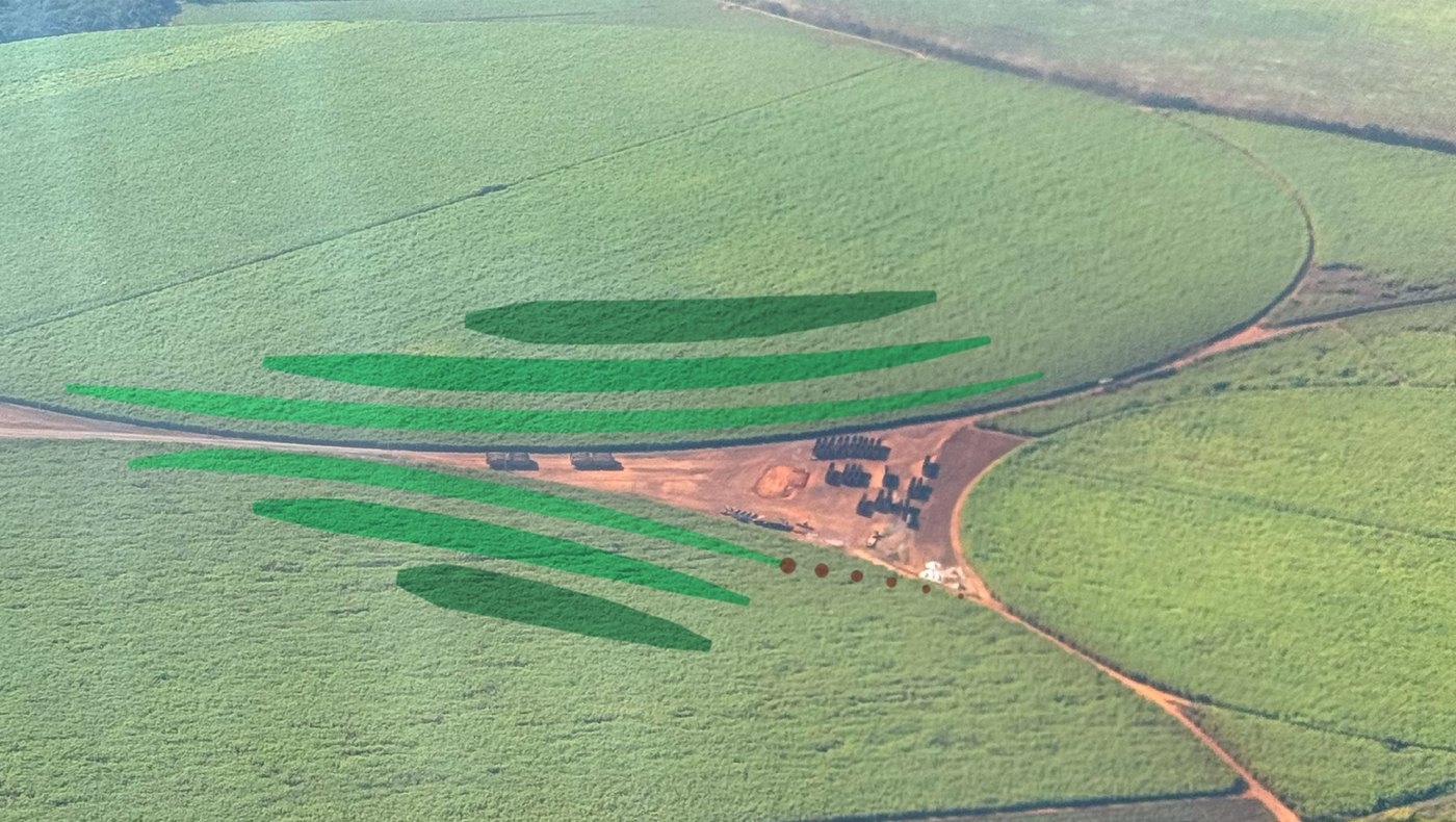 Vista aérea do canavial sob pivô central, com os arcos verdes e os pontos marrons do símbolo da marca desenhados por cima das linhas de plantio e da fileira de fornos