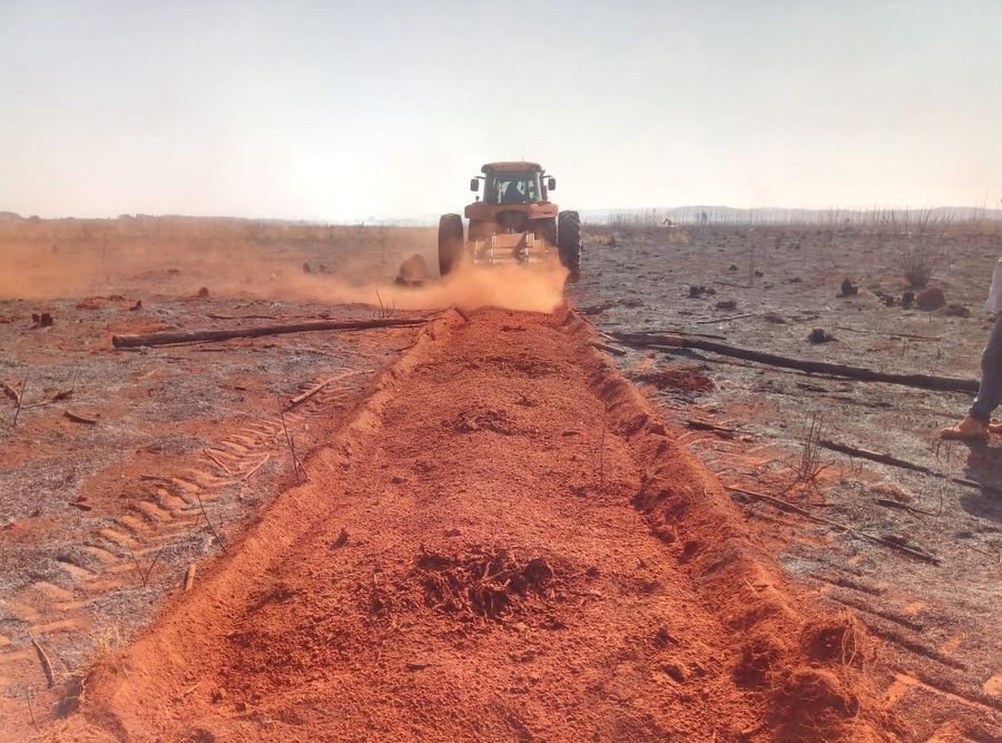Trator levantando poeira vermelha ao abrir uma leira de terra no campo